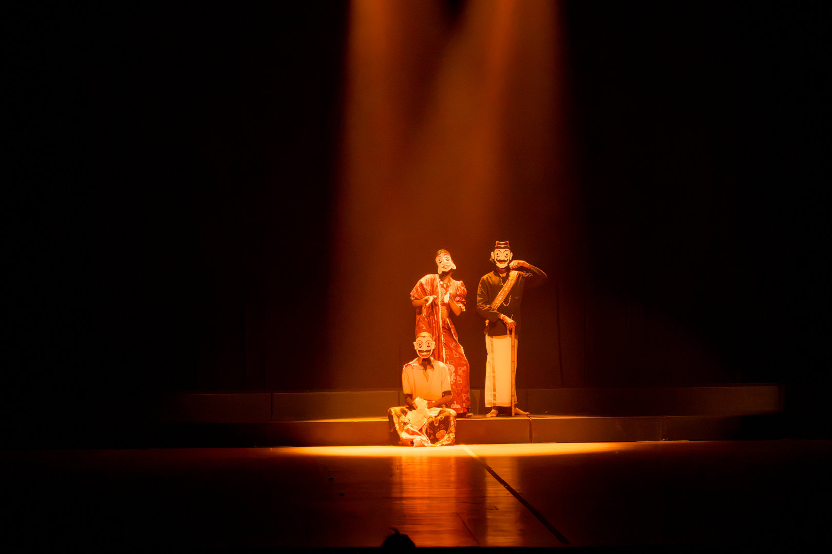 Three Actors in Mystical Spotlight on Traditional Stage Three actors in traditional costumes perform under a golden spotlight on a dark, dramatic stage.
