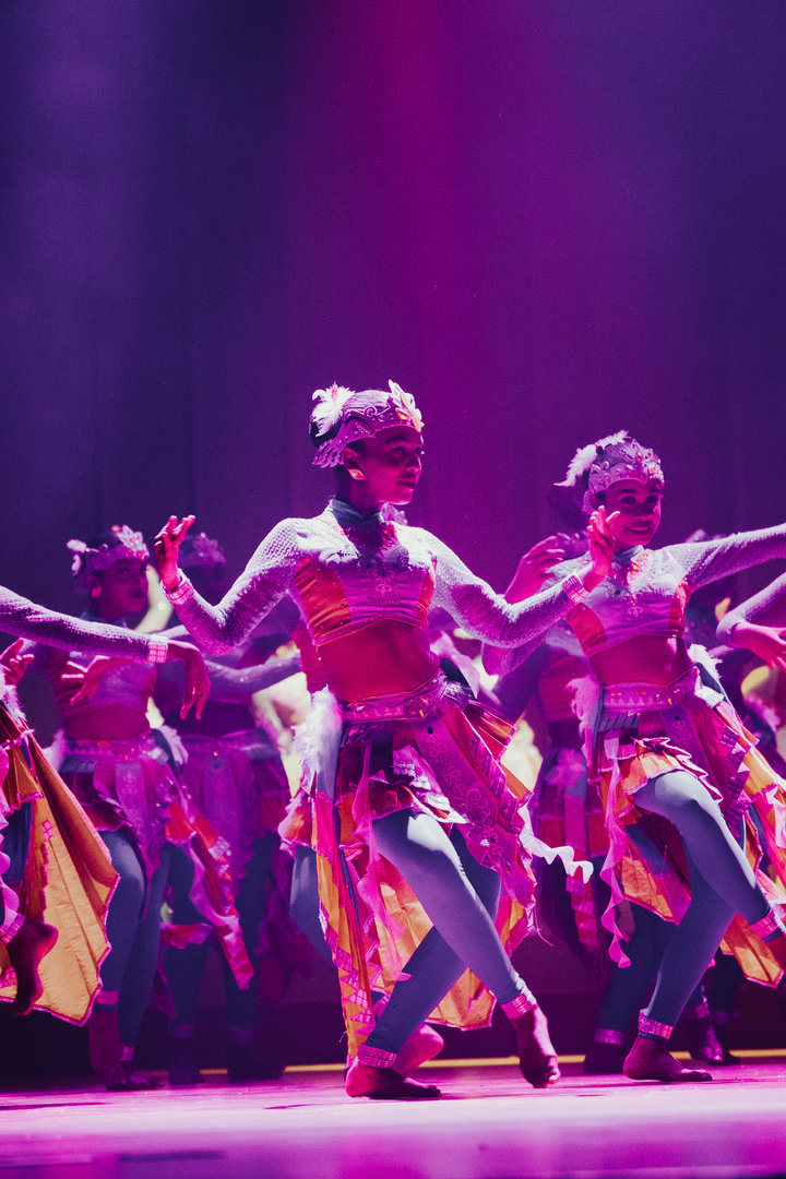 Colorful Folk Dance Performance Under Vibrant Stage Lights Dancers in colorful folk costumes perform energetically under vibrant magenta and purple stage lights.