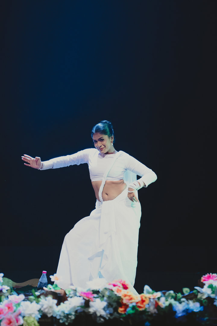 Elegant Classical Dancer in White With Vibrant Floral Stage Woman in white traditional dance costume performing on stage with colorful flowers and dark background.