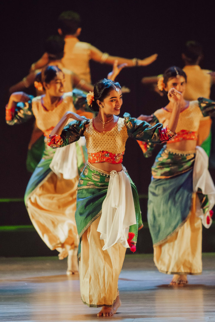 Vibrant Indian Classical Dance Troupe Performing on Stage Three women in elaborate Indian costumes performing a synchronized classical dance on a festival stage.