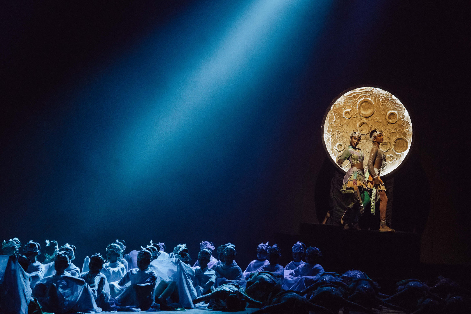 Moonlit Stage Fantasy With Dramatic Costumed Performers Theater scene with glowing moon, blue lighting, costumed performers, and mystical ensemble on stage.