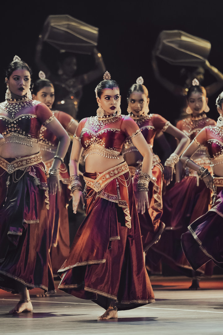 Graceful Bharatanatyam Dancers in Traditional Maroon and Gold Bharatanatyam dancers in maroon and gold costumes performing expressive poses on a dramatic stage.