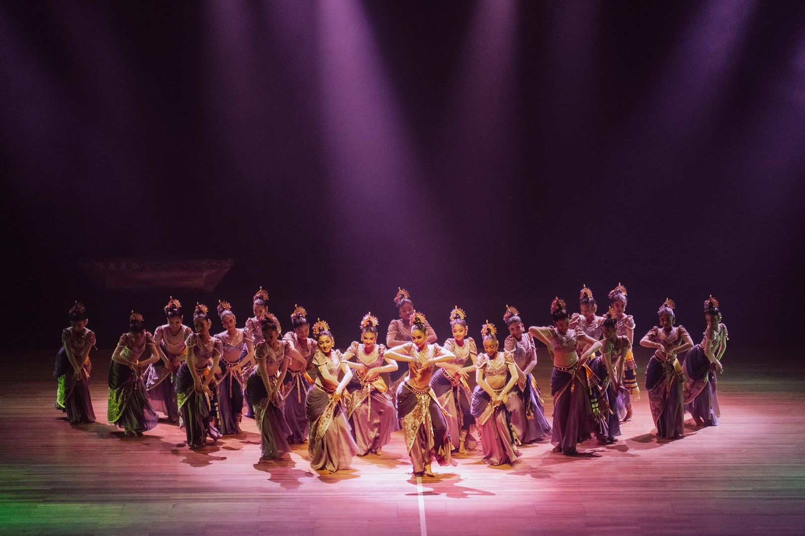 Vibrant Southeast Asian Dance Performance on Illuminated Stage Southeast Asian dancers in ornate costumes perform synchronized dance under dramatic purple stage lighting.