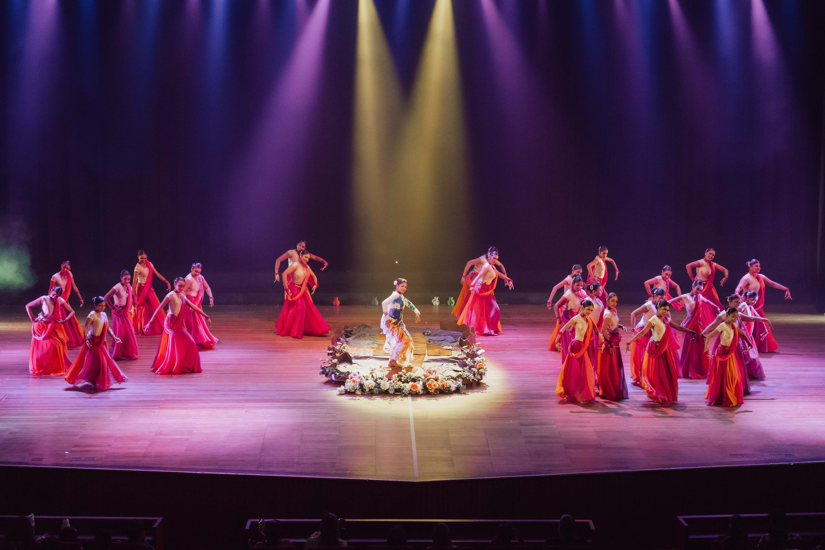 Vibrant Cultural Dance Performance With Dramatic Stage Lighting Dancers in red costumes perform a traditional ceremony under vibrant stage lighting and a central prop.