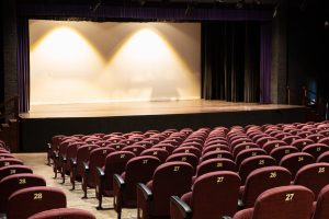 Elegant Theater Interior With Burgundy Seats and Lit Stage Classic theater interior with empty burgundy seats facing a lit stage, ready for a performance.