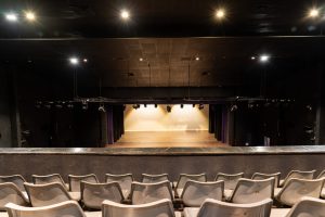 Modern Theater Auditorium Interior With Stage and Lighting Modern theater auditorium with gray seats, stage, lighting rig, and black ceiling, ready for performance.