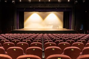 Empty Theater Stage Ready for Performance Empty theater with maroon seats, numbered rows, stage, curtains, and professional lighting ready for performance.