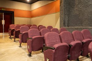 Modern Theater Auditorium With Maroon Seating and Exit Doors Modern auditorium with maroon seats, ergonomic design, labeled rows, concrete floor, and exit doors visible.